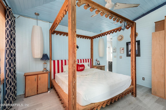 bedroom featuring lofted ceiling, light wood-style flooring, and wooden walls