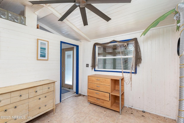 interior space with lofted ceiling with beams, wood walls, and a ceiling fan