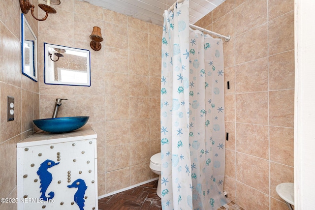 bathroom with vanity, a tile shower, toilet, and tile walls