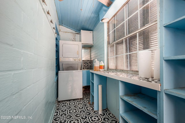 clothes washing area with concrete block wall, laundry area, wooden ceiling, and stacked washing maching and dryer