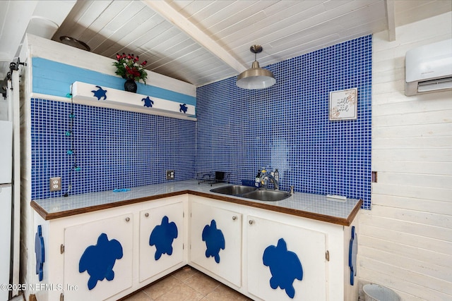 kitchen featuring light tile patterned floors, white cabinets, beamed ceiling, decorative light fixtures, and a sink