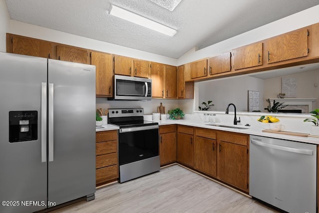 kitchen with brown cabinetry, lofted ceiling, appliances with stainless steel finishes, light countertops, and a sink