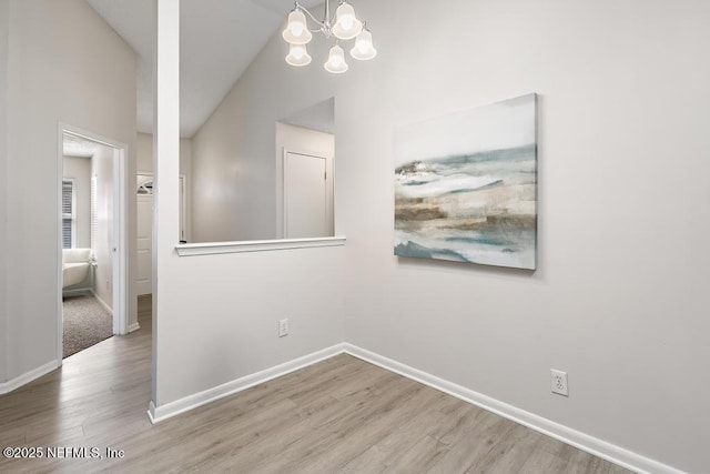 interior space with an inviting chandelier, vaulted ceiling, baseboards, and wood finished floors