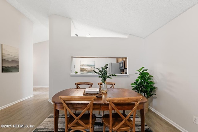 dining space featuring lofted ceiling, a textured ceiling, baseboards, and wood finished floors