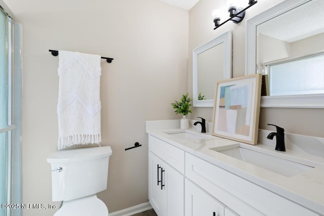 bathroom with double vanity, a shower with door, toilet, and a sink