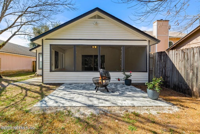 rear view of property featuring a fire pit, a patio area, fence, and a sunroom