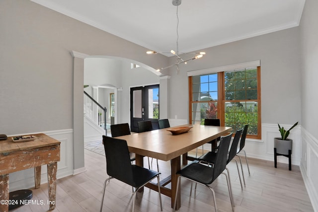 dining space featuring arched walkways, wainscoting, stairway, light wood-type flooring, and a chandelier