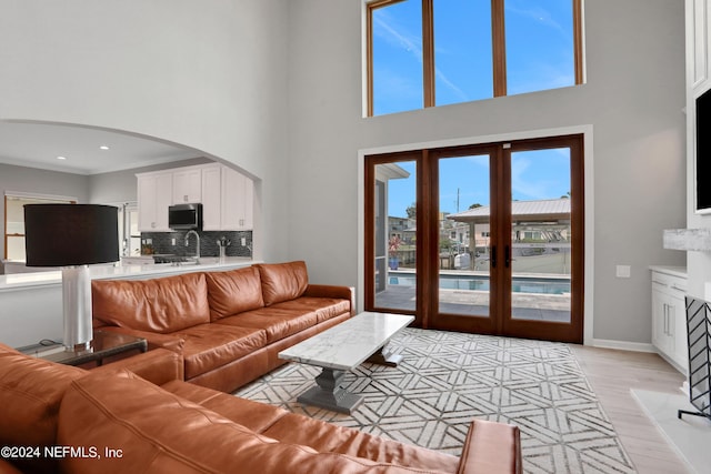 living room featuring arched walkways, light wood finished floors, a high ceiling, ornamental molding, and baseboards