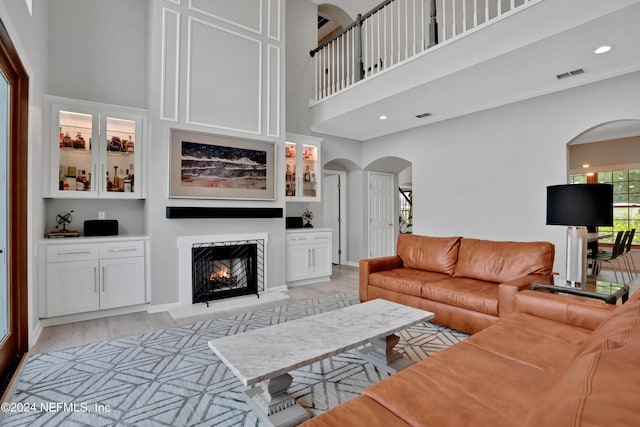 living room with arched walkways, a towering ceiling, visible vents, and light wood-style floors