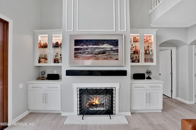 bar featuring a fireplace with flush hearth, arched walkways, baseboards, and light wood finished floors