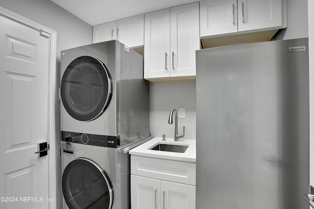 washroom featuring stacked washer and clothes dryer, cabinet space, and a sink