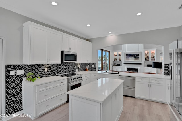 kitchen featuring a peninsula, a sink, white cabinetry, light wood-style floors, and appliances with stainless steel finishes