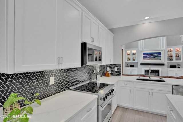 kitchen featuring stainless steel appliances, a sink, white cabinets, light stone countertops, and tasteful backsplash