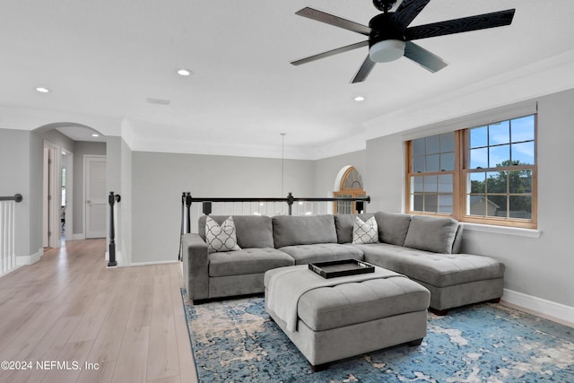 living area featuring arched walkways, light wood finished floors, crown molding, and baseboards