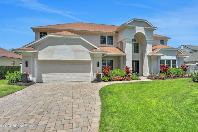 mediterranean / spanish-style home featuring a front lawn, decorative driveway, an attached garage, and stucco siding