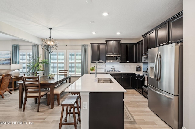 kitchen with stainless steel appliances, light countertops, hanging light fixtures, backsplash, and an island with sink