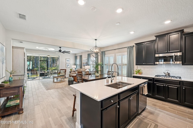 kitchen with stainless steel appliances, light countertops, backsplash, open floor plan, and a sink