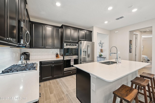 kitchen with stainless steel appliances, a sink, visible vents, light countertops, and backsplash