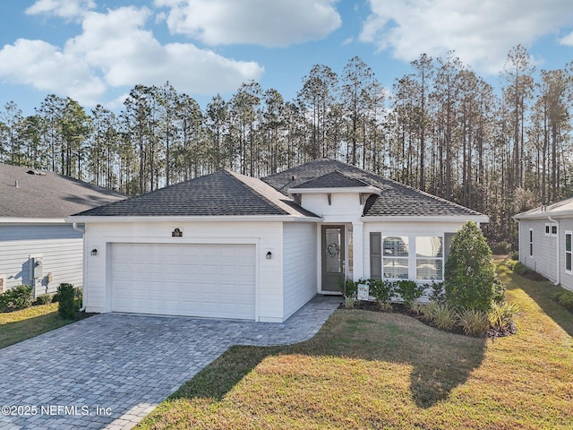 ranch-style home featuring a shingled roof, decorative driveway, an attached garage, and a front yard