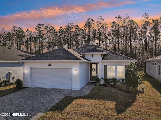 ranch-style home featuring decorative driveway, a garage, a front yard, and a shingled roof