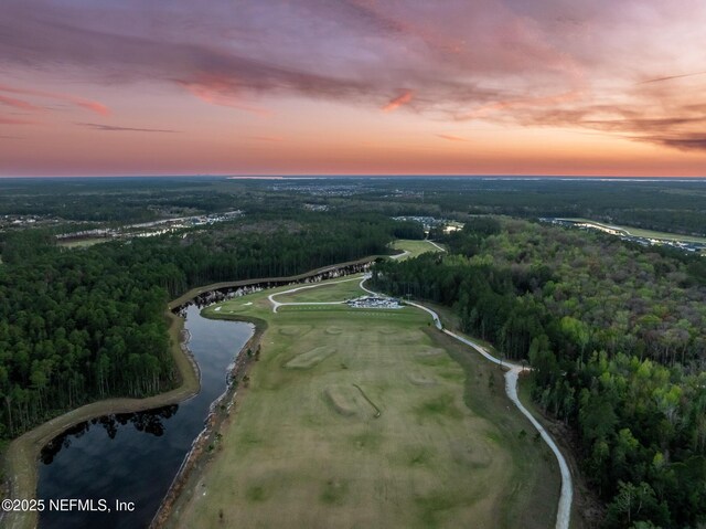 aerial view at dusk featuring a wooded view and a water view