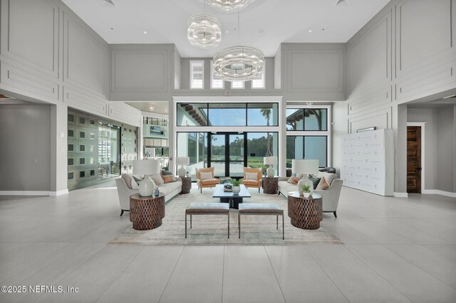 living area featuring light tile patterned flooring, baseboards, a notable chandelier, and a high ceiling