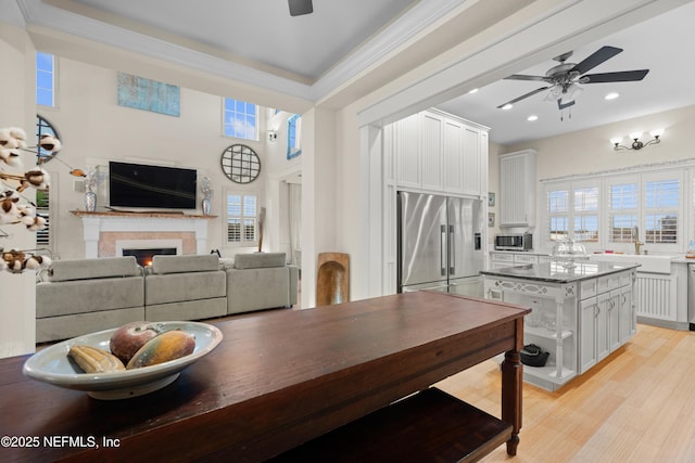 dining area featuring ceiling fan, a warm lit fireplace, recessed lighting, ornamental molding, and light wood-type flooring