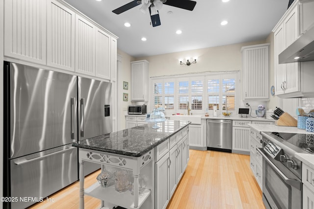 kitchen with wall chimney exhaust hood, white cabinetry, a kitchen island, and appliances with stainless steel finishes