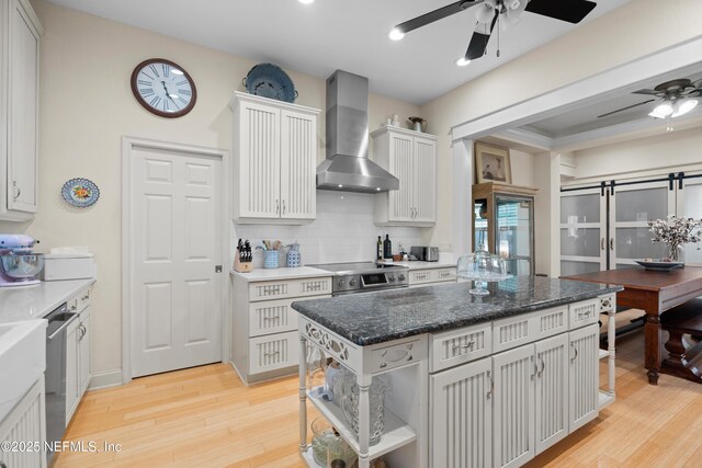 kitchen with stainless steel appliances, decorative backsplash, white cabinets, light wood-type flooring, and wall chimney exhaust hood