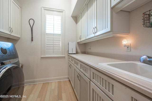 laundry room with light wood finished floors, cabinet space, a sink, washer / dryer, and baseboards