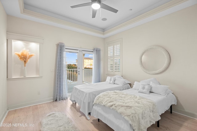 bedroom with access to outside, a tray ceiling, and light wood-style floors