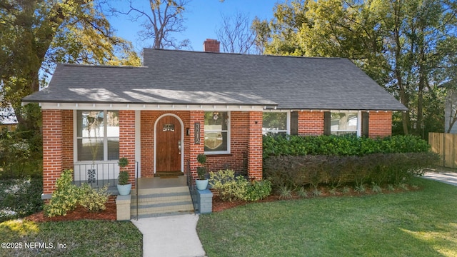 view of front of property with roof with shingles, a chimney, a front lawn, and brick siding