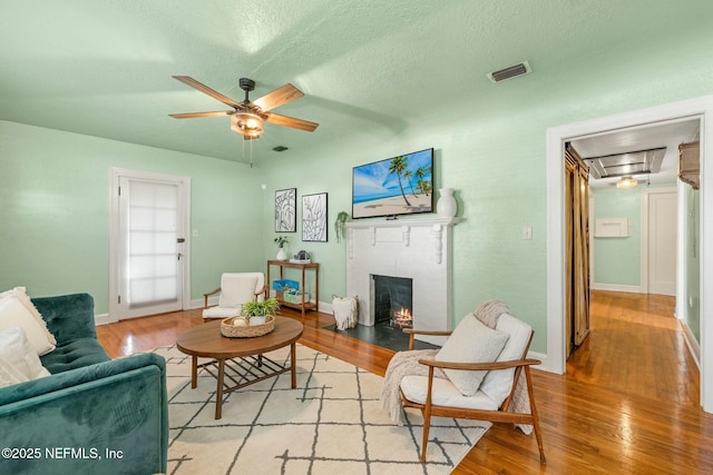 living area featuring a fireplace, visible vents, light wood-style floors, ceiling fan, and baseboards