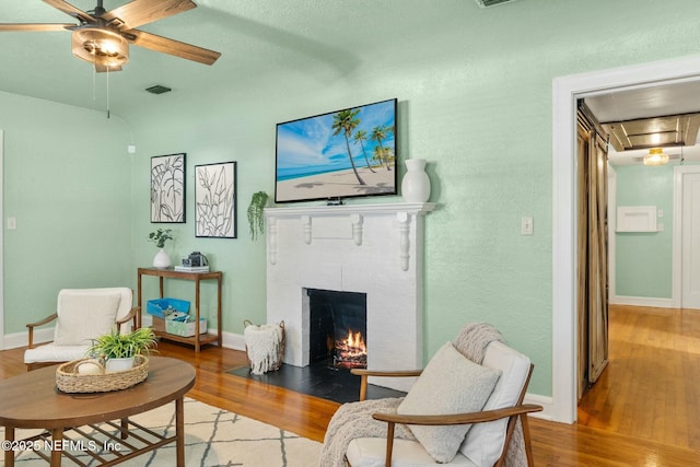 living area featuring visible vents, attic access, a ceiling fan, a fireplace with flush hearth, and wood finished floors