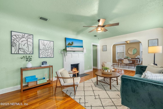 living room with arched walkways, light wood-style flooring, a fireplace with flush hearth, and visible vents