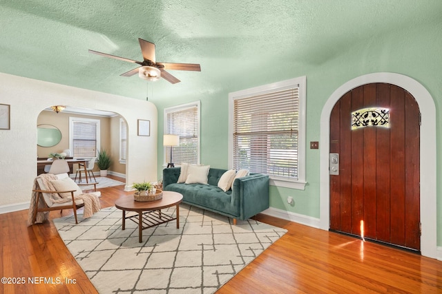 living room with light wood finished floors, ceiling fan, arched walkways, and a textured ceiling