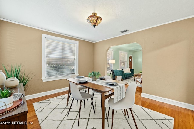 dining space with arched walkways, wood finished floors, visible vents, and baseboards