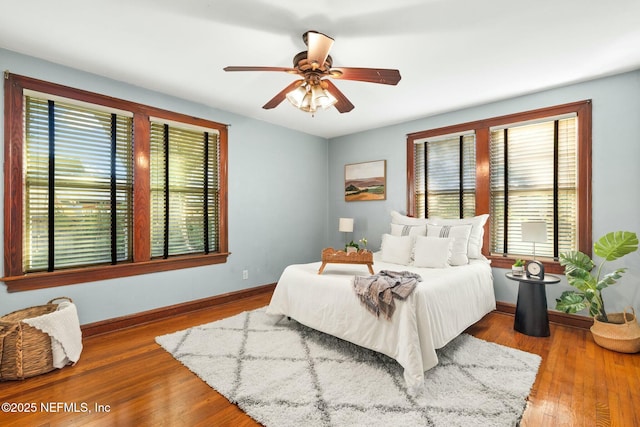 bedroom with a ceiling fan, multiple windows, baseboards, and wood finished floors