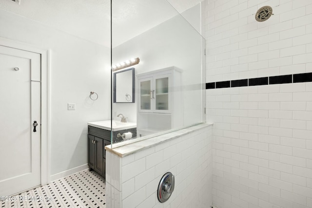 bathroom featuring a tile shower, vanity, and baseboards