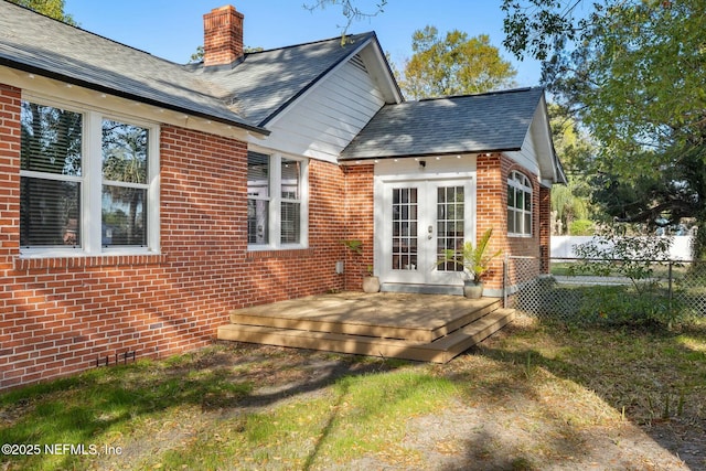 rear view of property featuring french doors, a chimney, fence, and brick siding