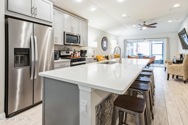 kitchen with a breakfast bar, light countertops, appliances with stainless steel finishes, a kitchen island with sink, and a sink