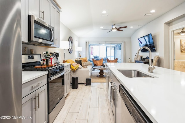 kitchen featuring light countertops, gray cabinetry, appliances with stainless steel finishes, open floor plan, and a sink