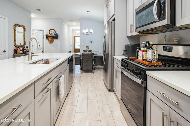 kitchen with decorative light fixtures, gray cabinets, light countertops, appliances with stainless steel finishes, and a sink