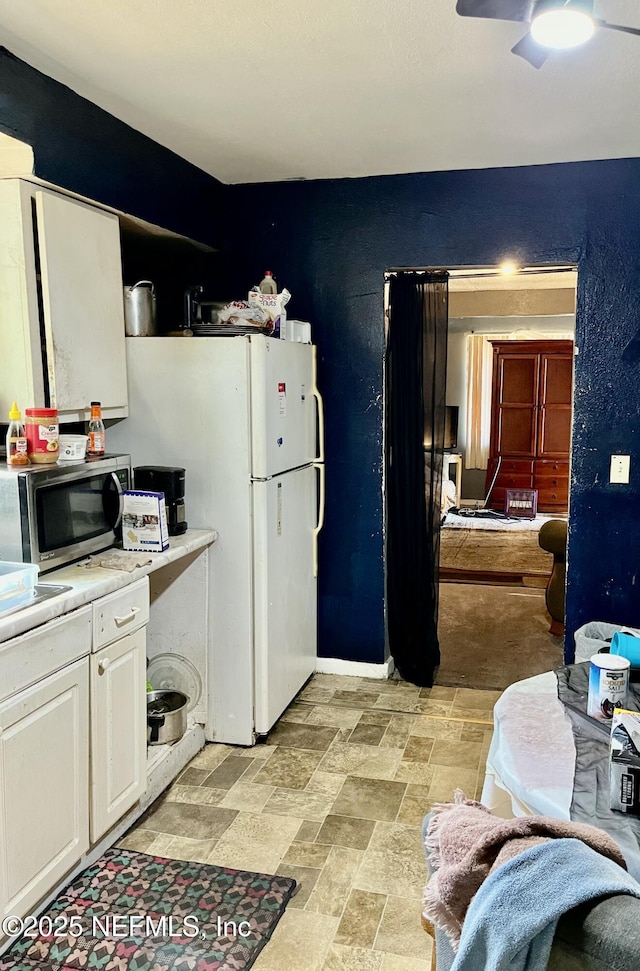 kitchen with light countertops, stainless steel microwave, freestanding refrigerator, stone finish flooring, and white cabinets