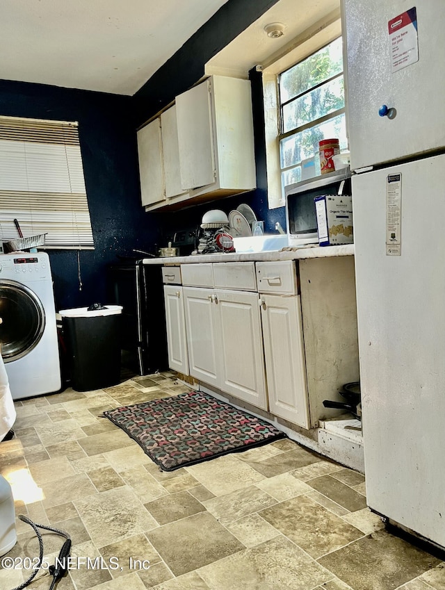 kitchen with washer / clothes dryer, light countertops, freestanding refrigerator, stone finish floor, and white cabinetry