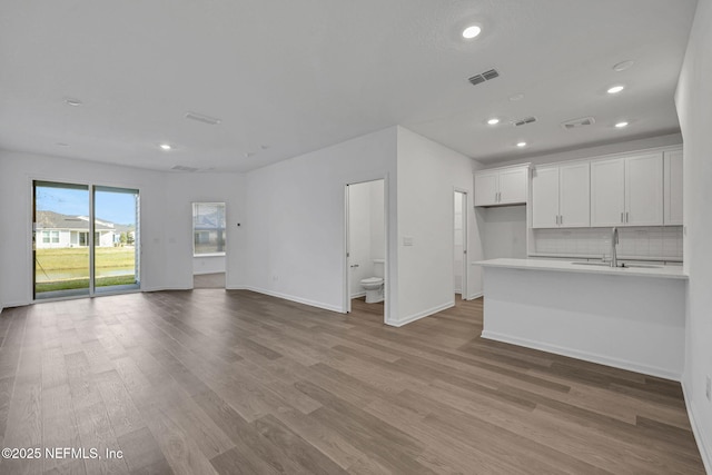 unfurnished living room featuring light wood-style floors, visible vents, a sink, and baseboards