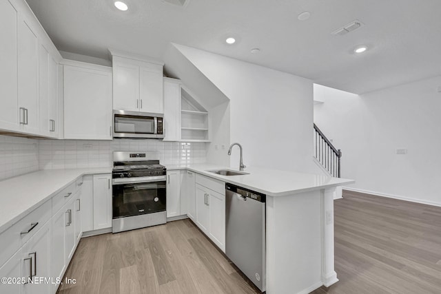 kitchen featuring stainless steel appliances, a peninsula, a sink, white cabinets, and light countertops