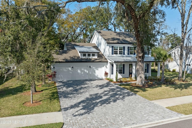 view of front of house featuring an attached garage, metal roof, a front lawn, and decorative driveway