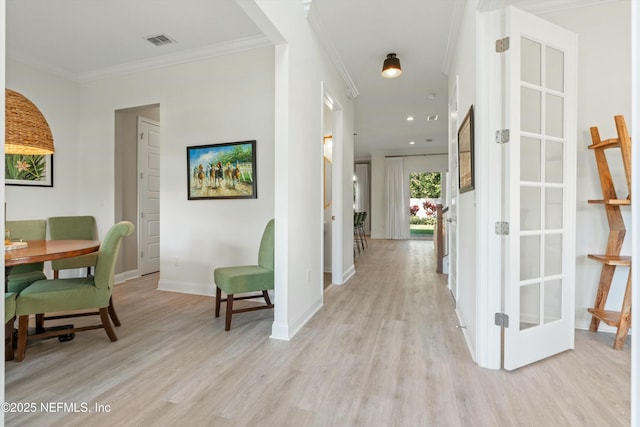 hallway featuring ornamental molding, light wood-style flooring, visible vents, and baseboards