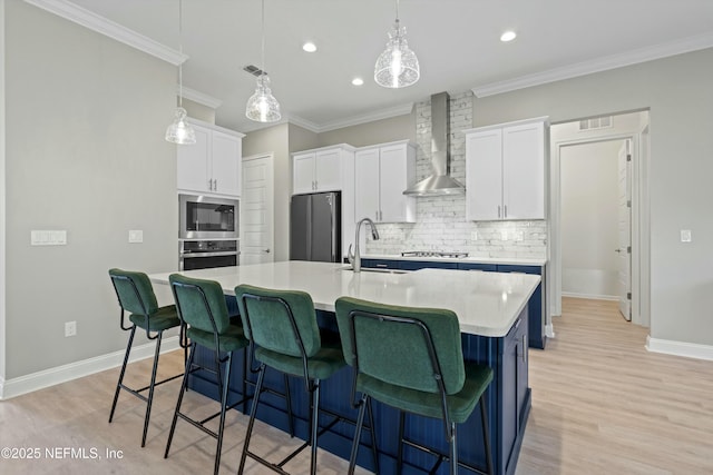 kitchen with visible vents, appliances with stainless steel finishes, a kitchen island with sink, wall chimney range hood, and white cabinetry